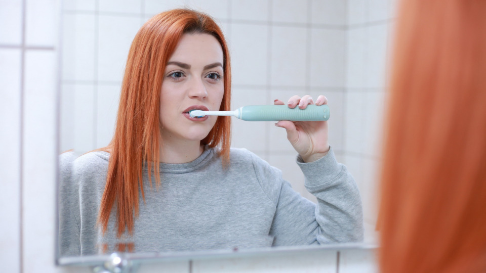 Professionelle Zahnreinigung: Eine junge rothaarige Frau putzt vor einem Spiegel ihre Zähne.