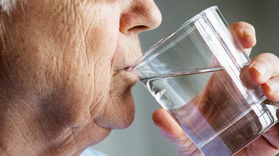 Eine ältere Dame trinkt ein Glas Wasser