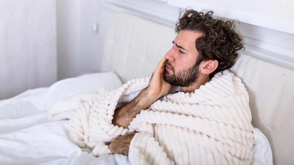 Ein Mann mit Zahnschmerzen im Bett